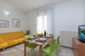 A dining area with a table set for two, a yellow sofa, green chairs, and a television on a stand. - Porto Letizia Leoncavallo 10, Porlezza, Italy (Porlezza)