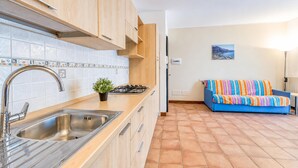 A kitchen with a sink, stove, and cabinets, a tiled backsplash, and a blue sofa in the adjacent living area. - Porto Letizia Bologna 4, Porlezza, Italy (Porlezza)