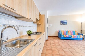A kitchen with a sink, stove, and cabinets, a tiled backsplash, and a blue sofa in the adjacent living area.