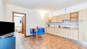 A modern kitchen with wooden cabinets, a microwave, and a dining area with blue chairs. - Porto Letizia Bologna 4, Porlezza, Italy (Porlezza)