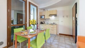 A compact kitchen with a dining area, featuring a wooden table, green chairs, and a microwave. - Porto Letizia Bach 7, Porlezza, Italy (Porlezza)