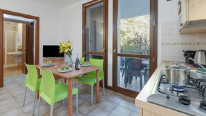A modern kitchen with a gas stove, a dining table with chairs, and a view through a glass door to an outdoor area. - Porto Letizia Bach 7, Porlezza, Italy (Porlezza)