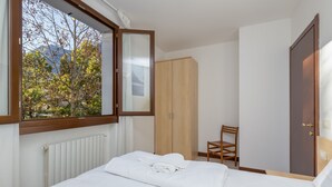 A bedroom with a bed, a wooden wardrobe, a chair, and a window with a view of trees and mountains. - Porto Letizia Bach 7, Porlezza, Italy (Porlezza)