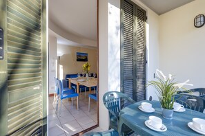 Zona pranzo con tavolo apparecchiato per quattro persone, sedie blu e una pianta in vaso.