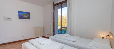 Ein Hotelzimmer mit zwei Betten, Meerblick, einem Bild an der Wand und einem Fenster mit Vorhängen.