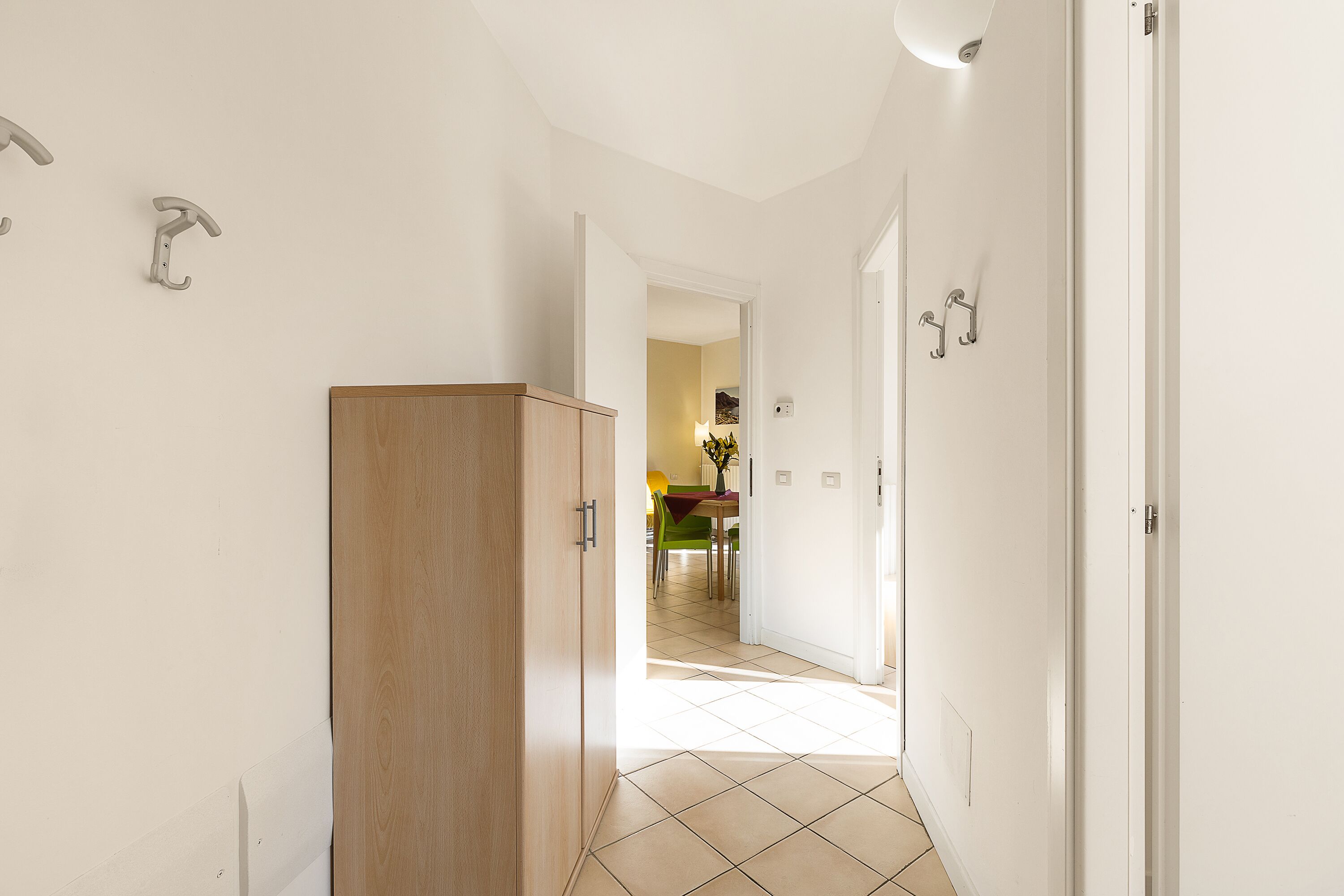 Ein Flur mit einem Holzschrank, weißen Wänden und einem gefliesten Boden, der zu einem Essbereich mit Tisch und Stühlen führt.