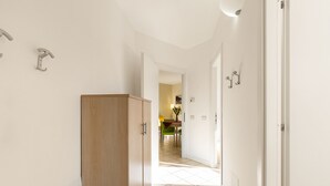 Un couloir avec une armoire en bois, des murs blancs et un sol carrelé, qui mène à un coin repas avec une table et des chaises.