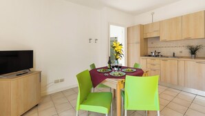 Une cuisine moderne avec des meubles en bois, une table à manger recouverte d’une nappe rouge et des chaises vertes.