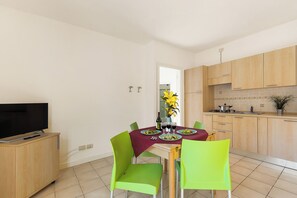 A modern kitchen with wooden cabinets, a dining table with a red tablecloth, and green chairs.