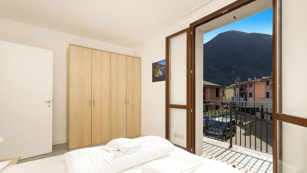A bedroom with a bed, a wooden wardrobe, and a balcony with a mountain view. - Porto Letizia Tchaikovsky 8, Porlezza, Italy (Porlezza)