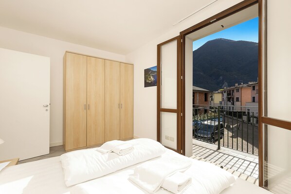 A bedroom with a bed, a wooden wardrobe, and a balcony with a mountain view.