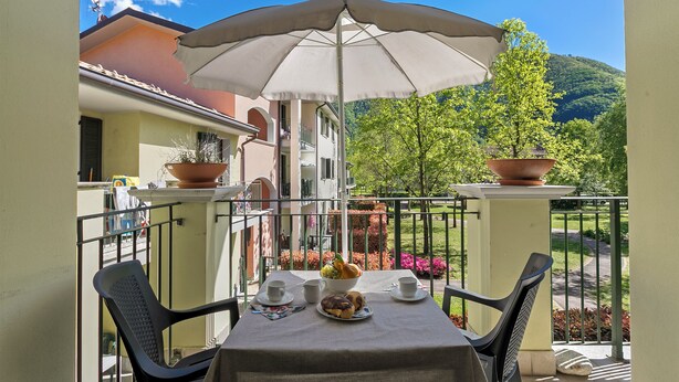 A balcony with a table set for breakfast, potted plants, and a view of the surrounding area. - Porto Letizia Ferrara 3, Porlezza, Italy (Porlezza)