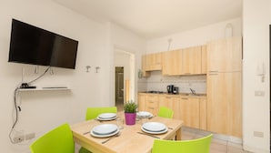 A dining area with a wooden table set for four, green chairs, and a flat-screen TV mounted on the wall.