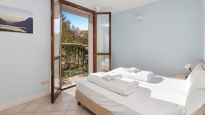 A bedroom with a bed, a painting, and a view of a garden through an open door.