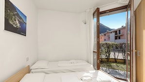 A hotel room with two beds, a large window with a view of buildings and mountains, and a painting on the wall.