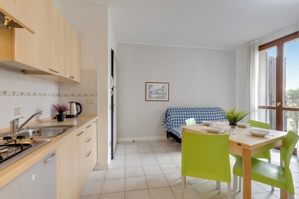 A compact kitchen with modern appliances, a dining area with a table and chairs, and a view through a window. - Porto Letizia Tchaikovsky 2, Porlezza, Italy (Porlezza)