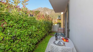 A small outdoor dining area with a table set for two, surrounded by lush greenery and a mountain in the background. - Porto Letizia Venezia 3, Porlezza, Italy (Porlezza)
