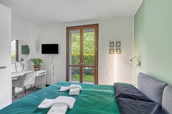A bedroom with a bed, a desk, a chair, a television, and a window with a view of greenery.