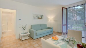 A modern living room with a light blue sofa, a small side table with a magazine, and a dining area with a table set for two. - Porto Letizia Mascagni 2, Porlezza, Italy (Porlezza)