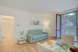 A modern living room with a light blue sofa, a small side table with a magazine, and a dining area with a table set for two.