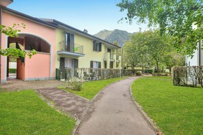 A residential building with a paved pathway, green lawns, and a mountain in the background.