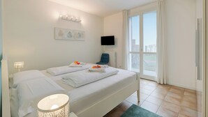 A hotel room with a bed, a chair, a TV, and a window with curtains. - Porto Letizia Mascagni 2, Porlezza, Italy (Porlezza)