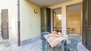 An outdoor dining area with a table set for breakfast, surrounded by chairs, and a building entrance with shutters.