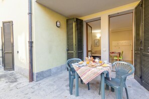 An outdoor dining area with a table set for breakfast, surrounded by chairs, and a building entrance with shutters.