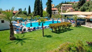 A pool area with lounge chairs and umbrellas, surrounded by greenery and buildings.