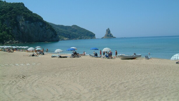 A beach with umbrellas and lounge chairs, a boat, and a rocky cliff in the background.