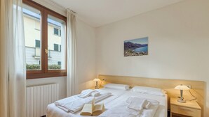 Habitación de hotel con cama, dos mesitas de noche, ventana con cortinas, un cuadro colgado en la pared y un radiador.