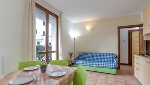 Un comedor con una mesa dispuesta para dos personas, un sofá verde y una kitchenette.
