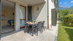 Een terras met een ontbijttafel, een keuken zichtbaar door een open deur, en een uitzicht op de bergen op de achtergrond.