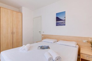 A hotel room with a bed, a wooden wardrobe, a door, a nightstand, and a wall-mounted picture. - Porto Letizia Bach 3, Porlezza, Italy (Porlezza)