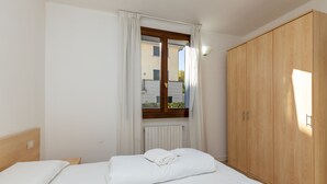 A bedroom with a bed, a wooden wardrobe, a window with curtains, and a radiator. - Porto Letizia Bach 1, Porlezza, Italy (Porlezza)