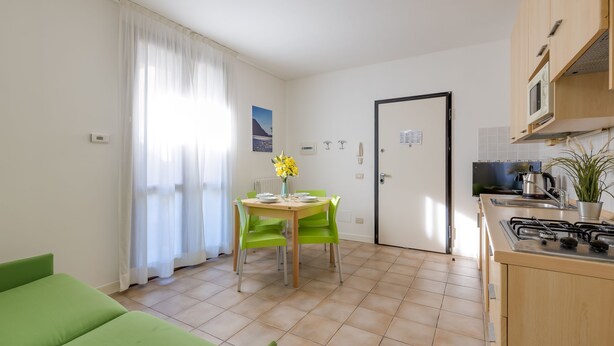 A compact kitchen with a dining area, a green sofa, and a white door. - Porto Letizia Bach 1, Porlezza, Italy (Porlezza)