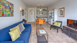 A living room with a blue sofa, a coffee table, and a TV stand. There is a dining area with a table and chairs. - Porto Letizia T5, Porlezza, Italy (Porlezza)