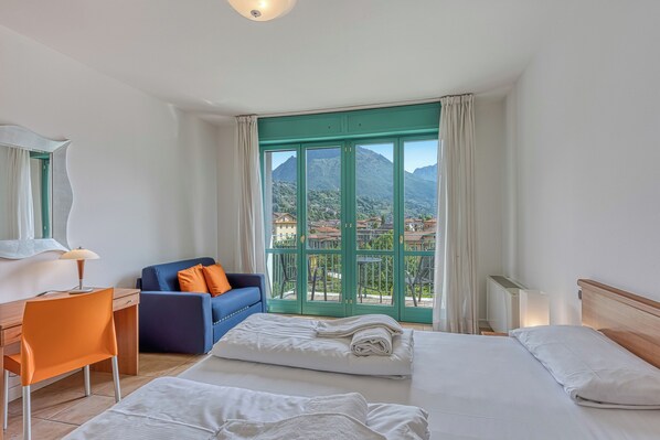 A hotel room with two beds, a desk, a chair, and a view of mountains.