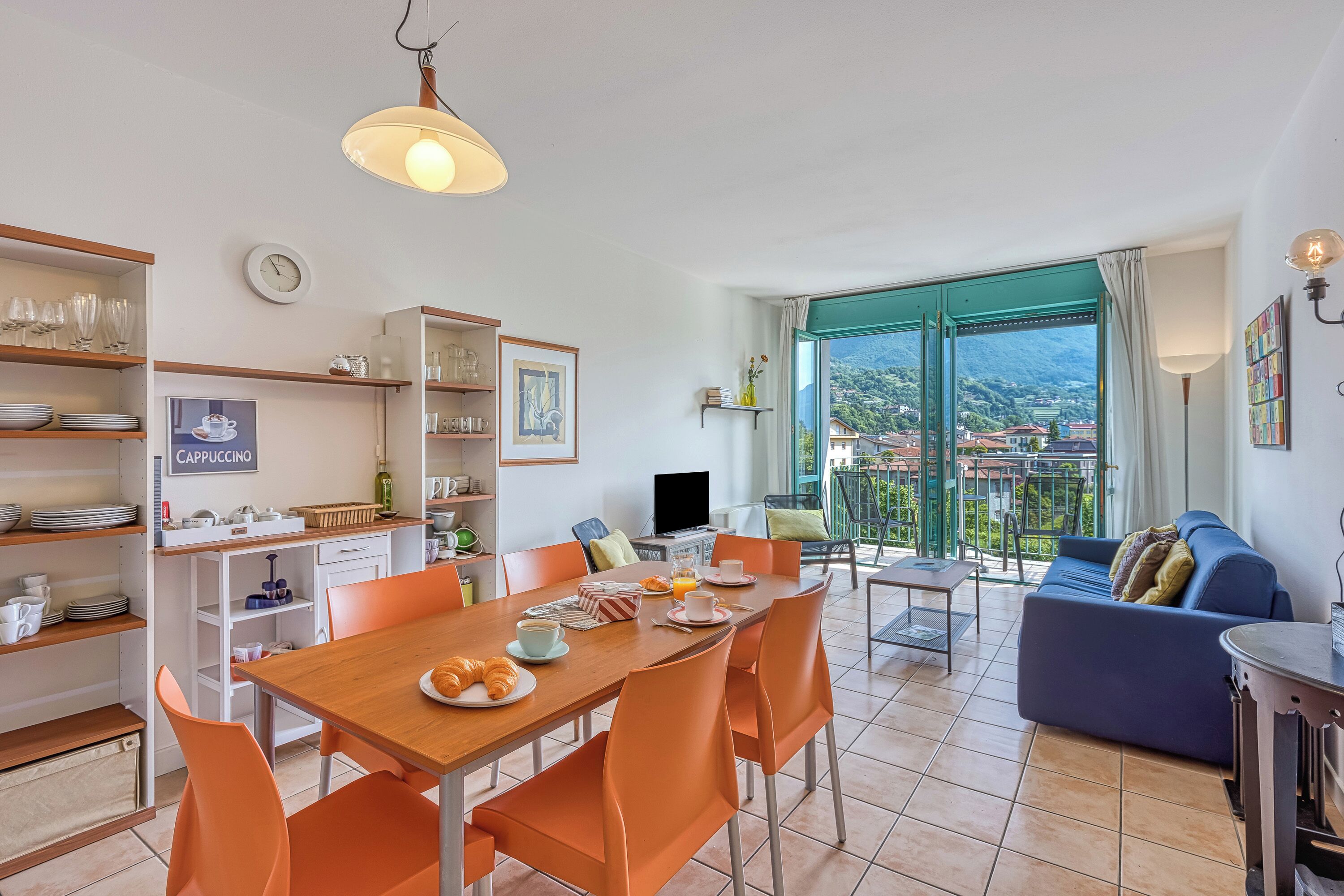 A modern kitchen with a dining area, a living room with a sofa, and a balcony with a view of the city.