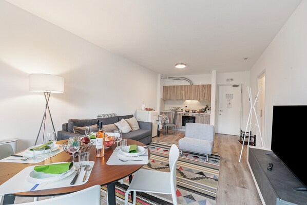 Een moderne woonkamer met een eethoek, een keuken op de achtergrond en een televisie aan de rechterkant.