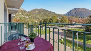 A balcony with a table set for two, overlooking a mountain and a road.