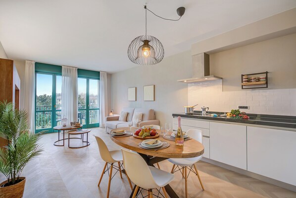 A modern kitchen with a dining area, large windows, and a view of greenery.