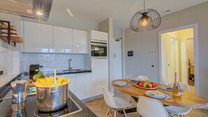 A modern kitchen with white cabinets, a built-in oven, and a dining area with a wooden table and white chairs. - Porto Letizia P18, Porlezza, Italy (Porlezza)