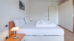 A neatly made bed with white linens, a bedside lamp, and a painting on the wall. - Porto Letizia P17, Porlezza, Italy (Porlezza)