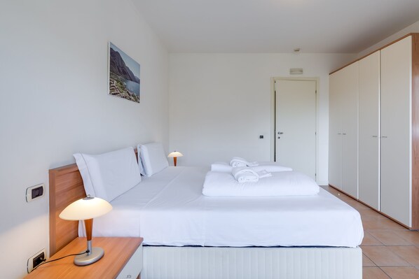 A neatly made bed with white linens, a bedside lamp, and a painting on the wall.