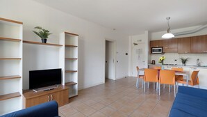 A modern living room with a flat-screen TV, a sofa, and a dining area with orange chairs. - Porto Letizia P17, Porlezza, Italy (Porlezza)