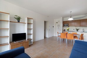 A modern living room with a flat-screen TV, a sofa, and a dining area with orange chairs.
