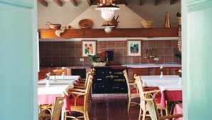 Un coin repas avec des chaises et des tables en bois, un lustre et des carreaux de cuisine en arrière-plan.