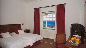 Une chambre d’hôtel avec un lit, un bureau sur lequel se trouve un panier de fruits, une télévision et une fenêtre donnant sur la mer.