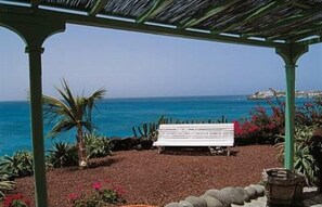 Un espace extérieur aménagé, abrité et doté d’un banc, de palmiers et d’une vue sur la mer.